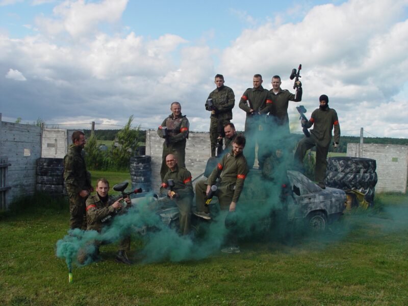 Grupa paintballowa w strojach moro w tle flara dymna.